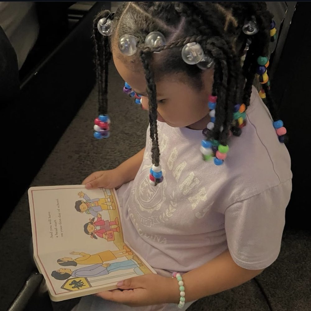 A little girl with beaded braids, absorbed in a picture book